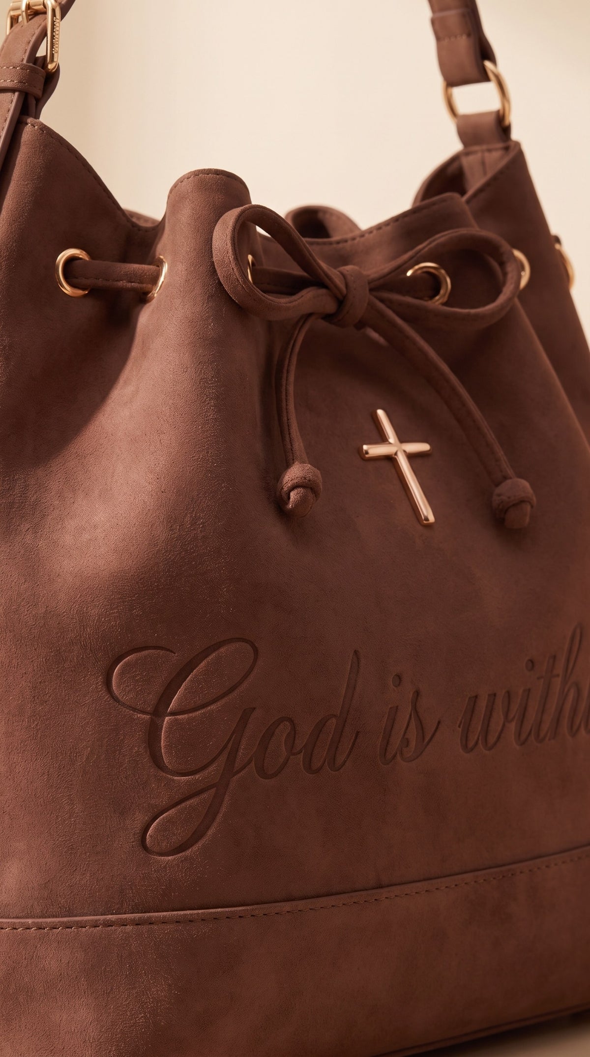 Close-up of the bow drawstring, rose-gold cross and debossed script on brown suede
